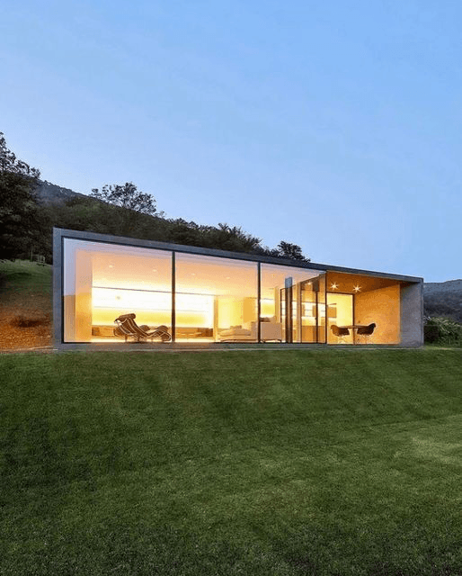 Glass-walled modern home glowing at dusk